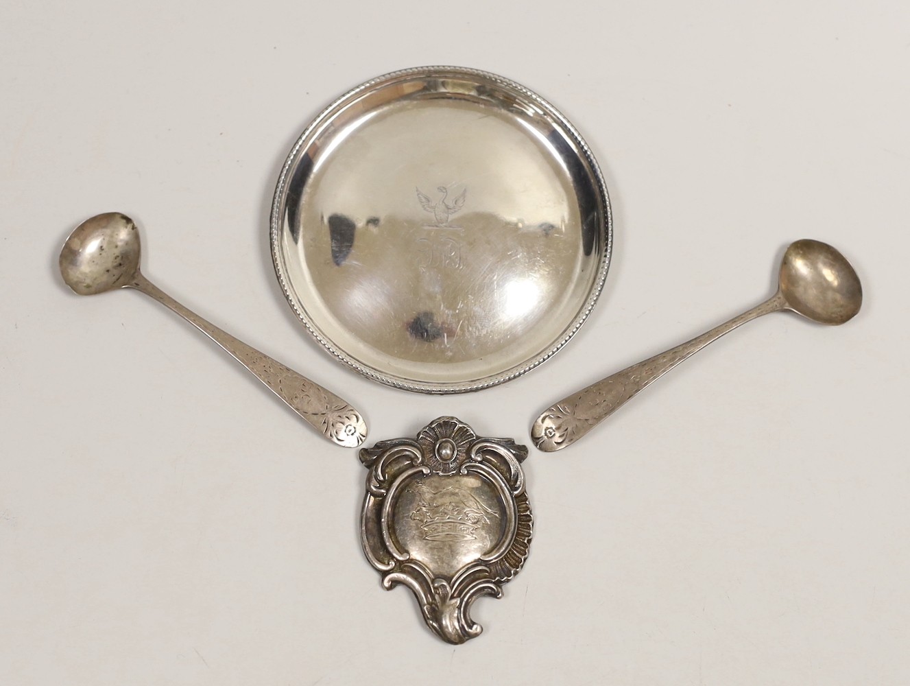 A George III silver glass coaster, William Plummer, London, 1781, 91mm, together with a pair of early 19th century Irish silver condiment spoons and a white metal cartouche.